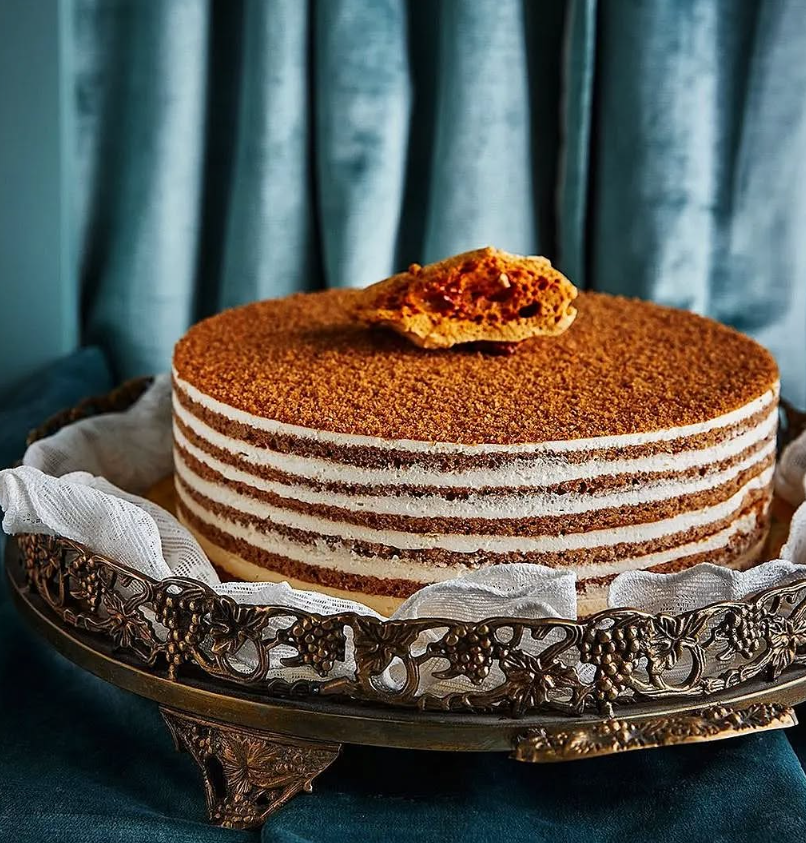 Layered honey cake on an ornate silver platter, set against a teal backdrop.