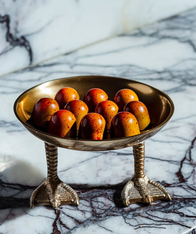 Gold bowl on bird-foot stand holding chocolate truffles, on marble surface.