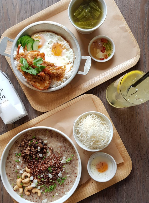 Two trays of food: fried egg with rice and soup, and rice porridge with toppings, alongside a lemonade.