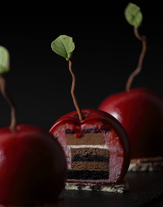 Cherry-shaped desserts, cut open to reveal layers of cake and mousse, with chocolate stems and leaves.