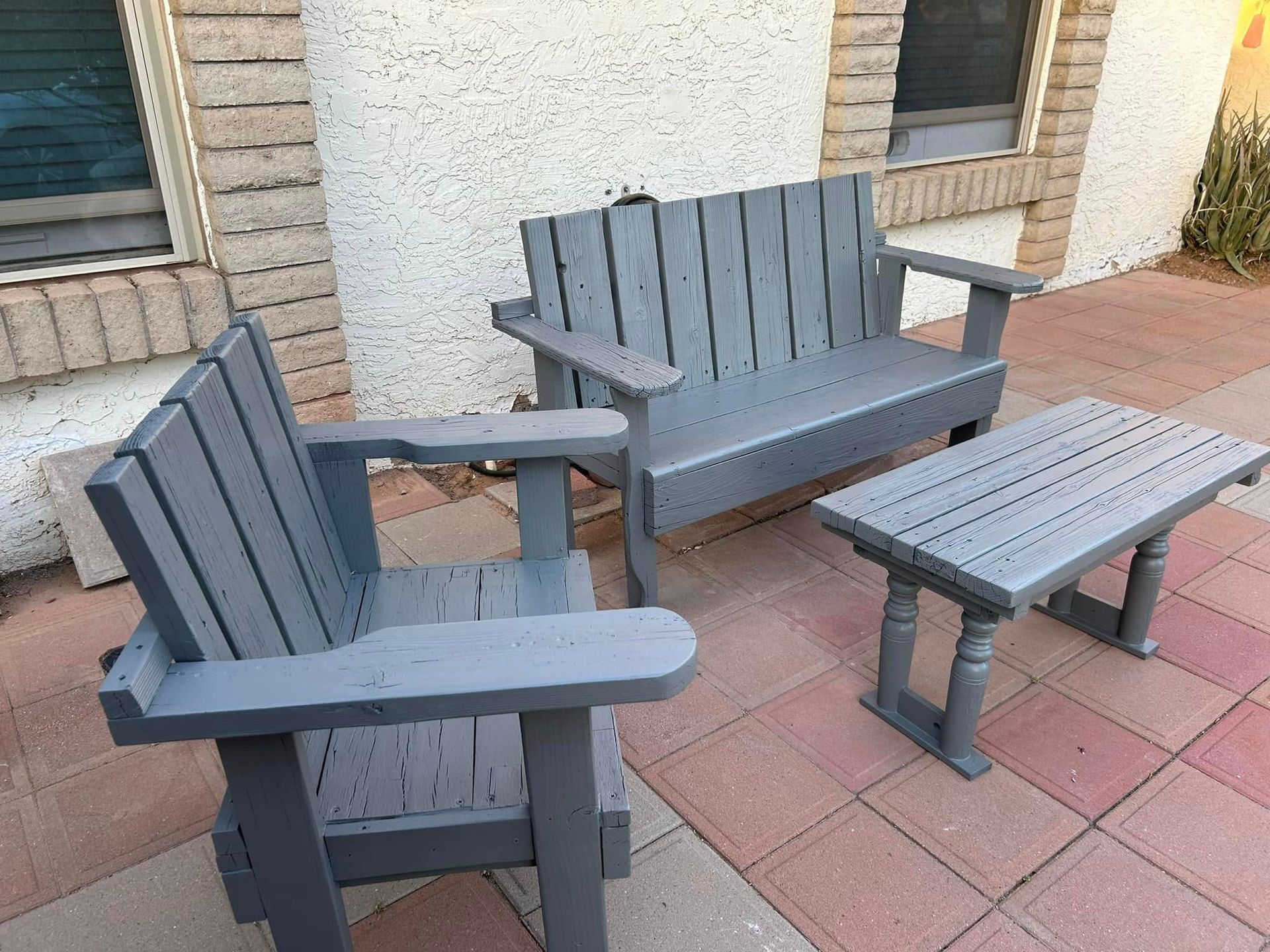 Gray Adirondack chair, bench, and small table set on a brick patio.