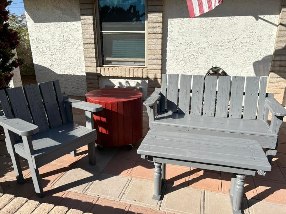 Gray wooden chairs and table on a porch next to a red barrel. American flag visible.