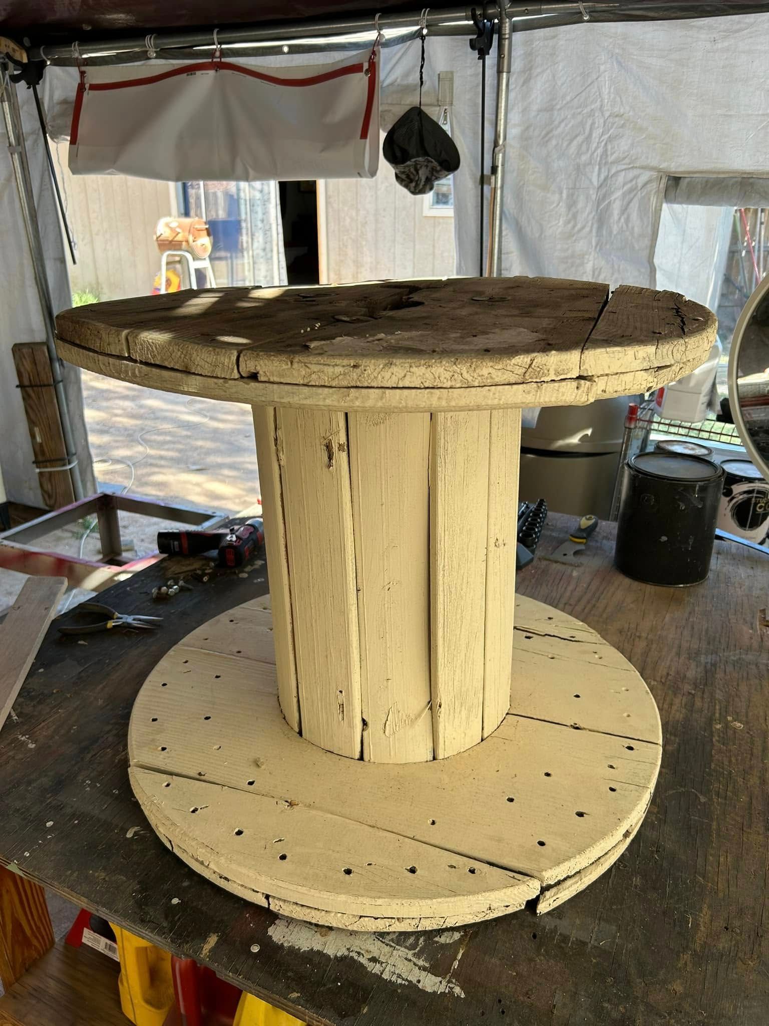 Wooden cable spool repurposed as a table, painted white, outdoors.