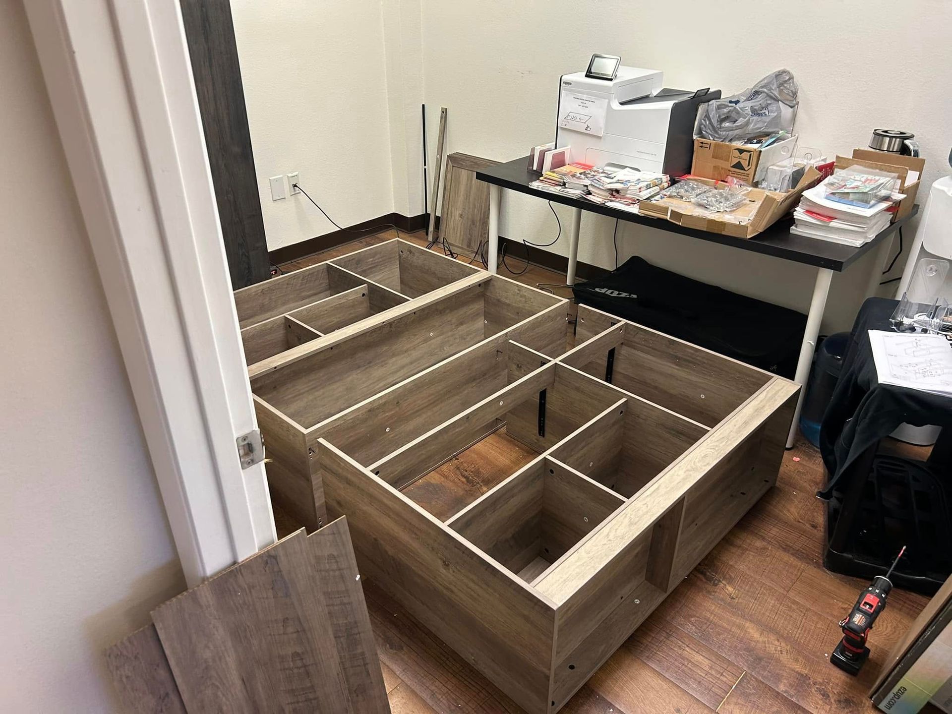 Two wooden storage units being assembled in a room, desk and debris in the background.