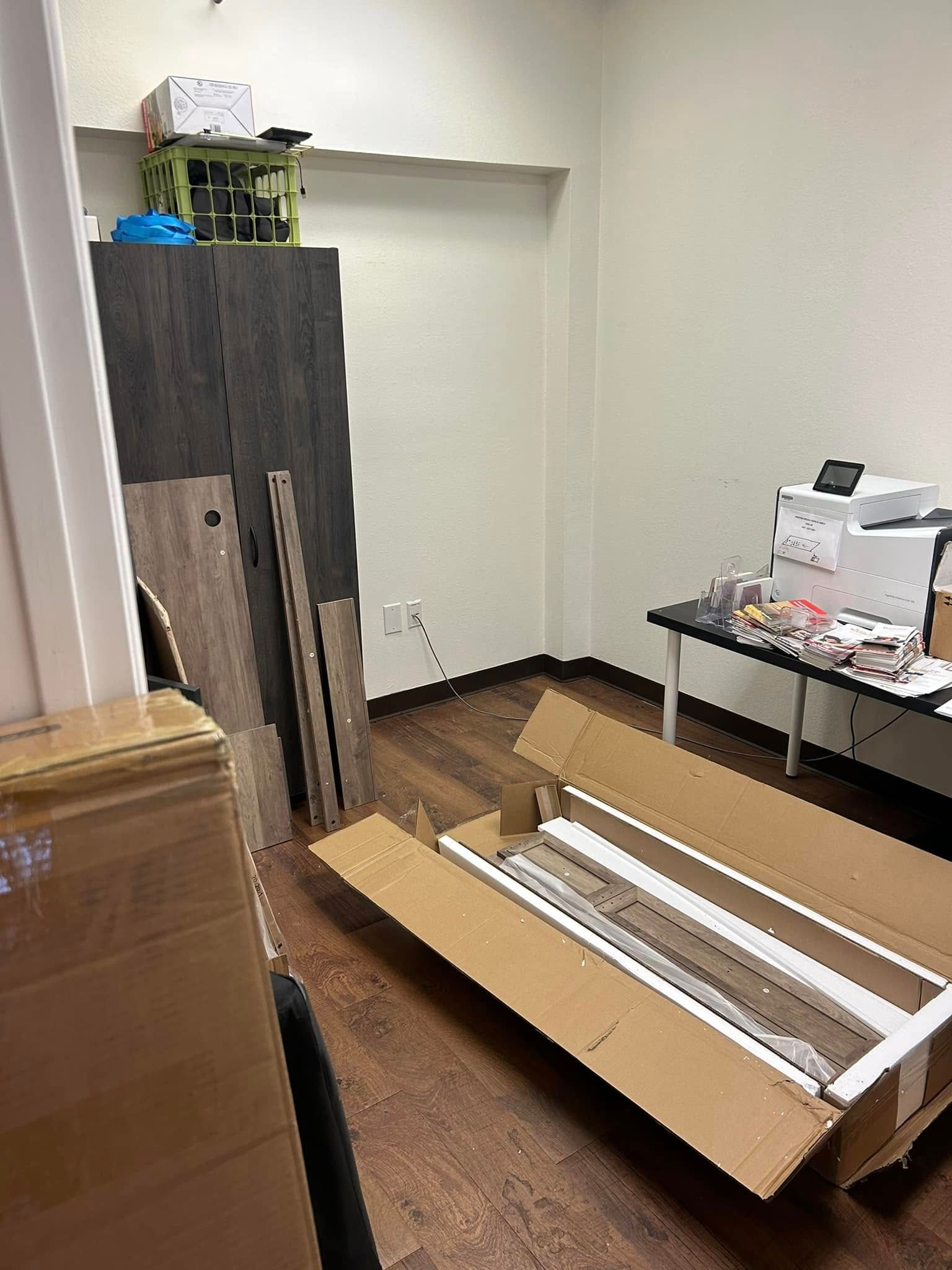 Room with unassembled furniture, cardboard boxes, and a desk with electronic components.