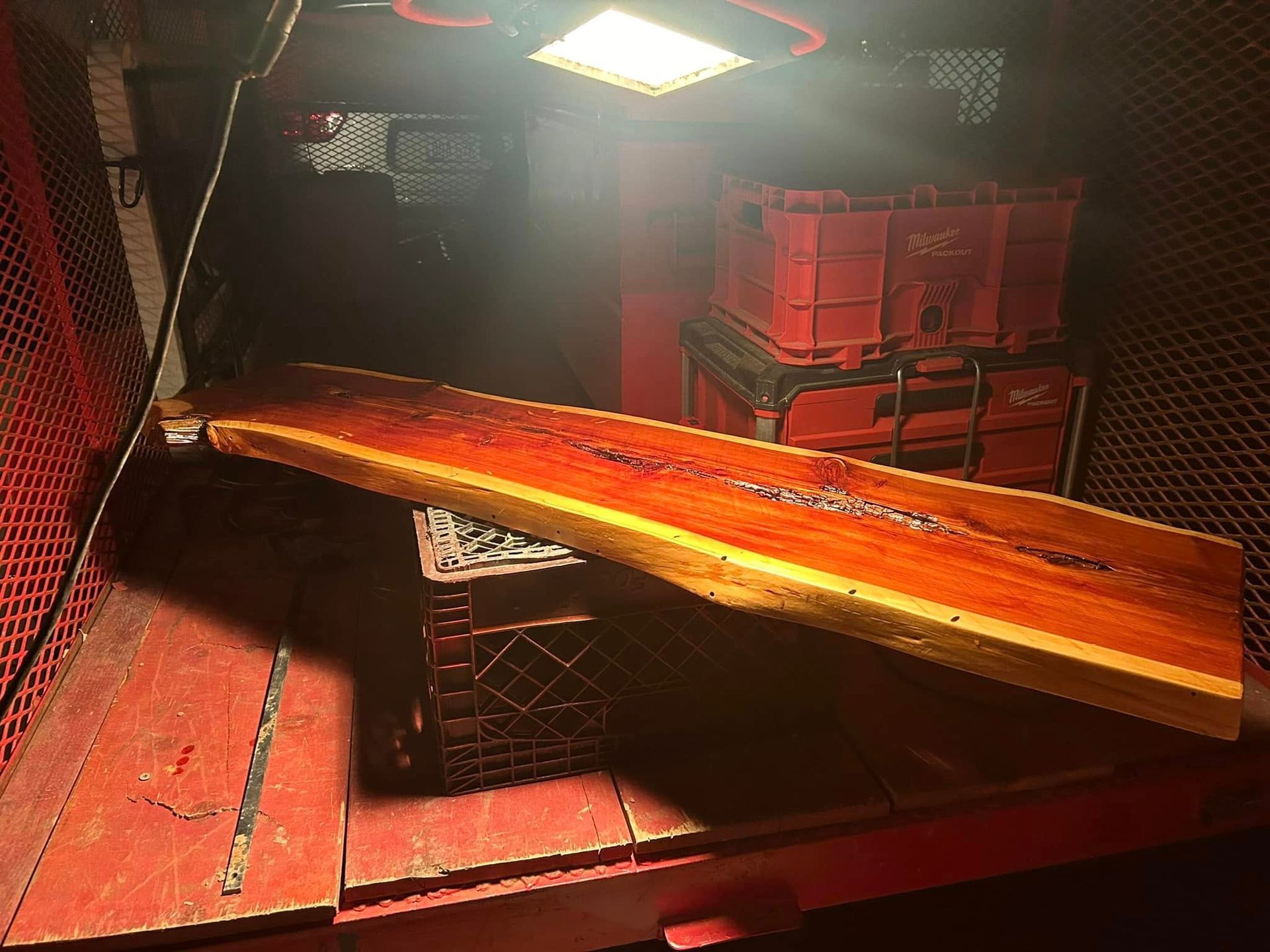 Wooden slab resting on a crate inside a red-walled storage area, illuminated by overhead light.