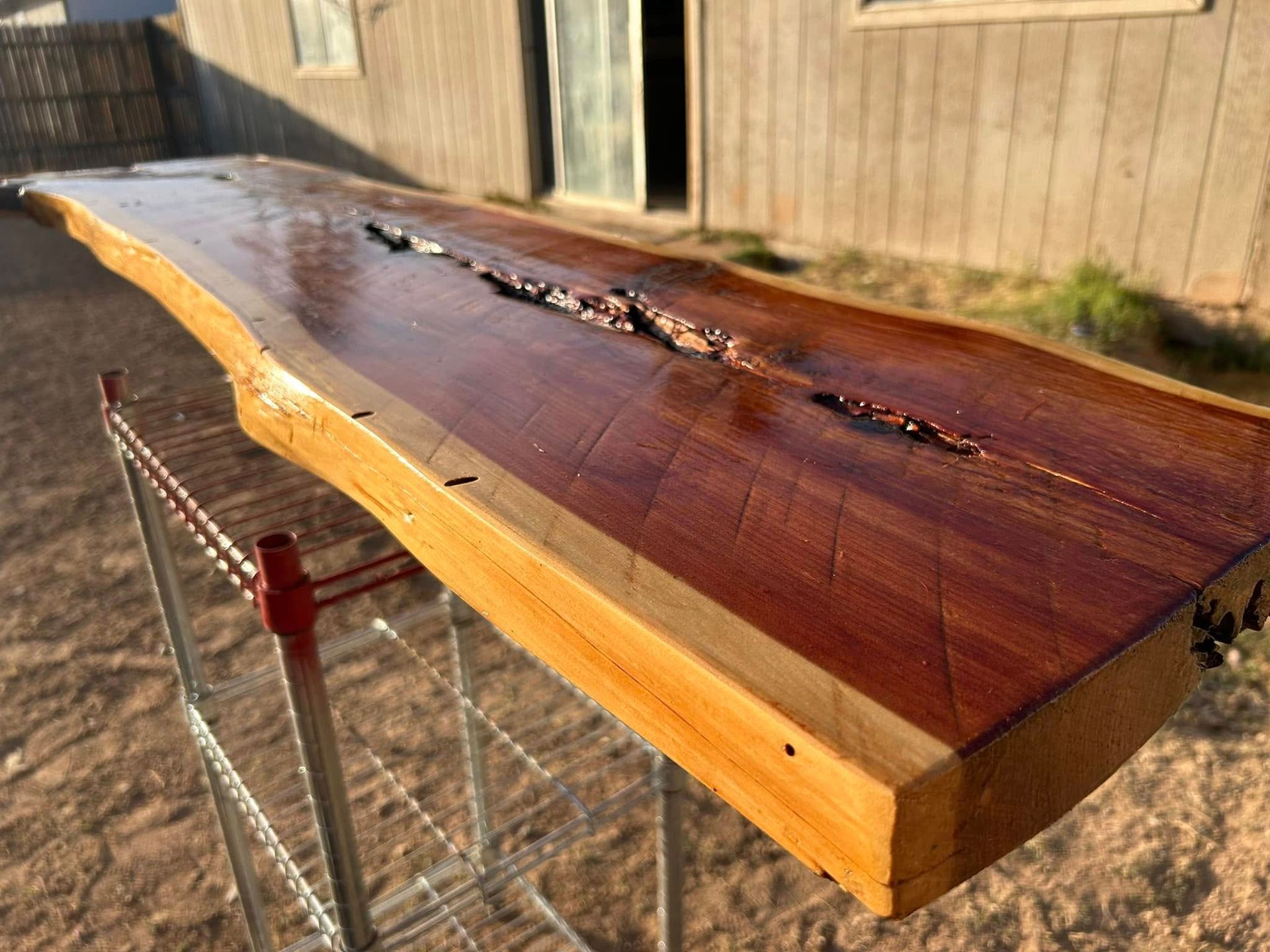 Live edge wooden table with a deep crack, resting on a metal stand, outside.