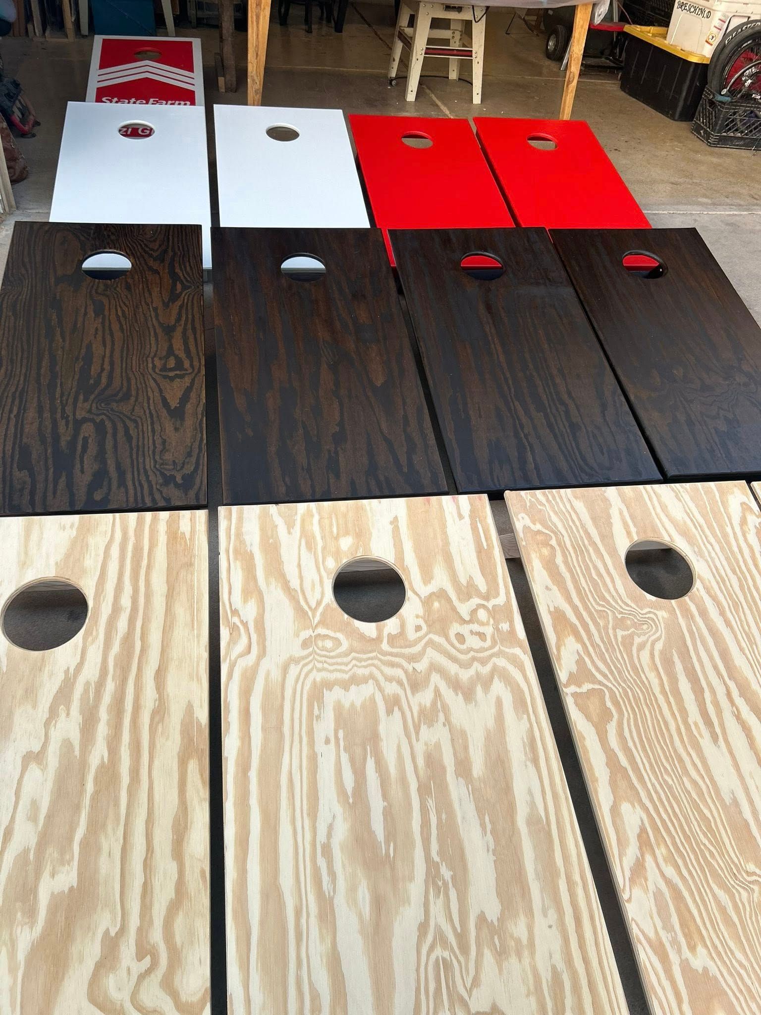 Cornhole boards of varying colors: red, white, dark brown, and natural wood, laid out on a surface.