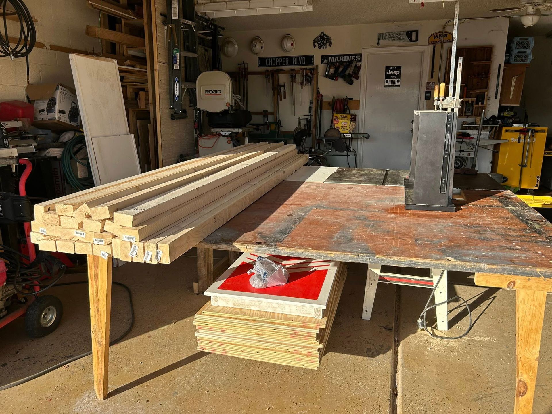 Garage workshop with lumber on a workbench. Boards, tools, and supplies are visible.