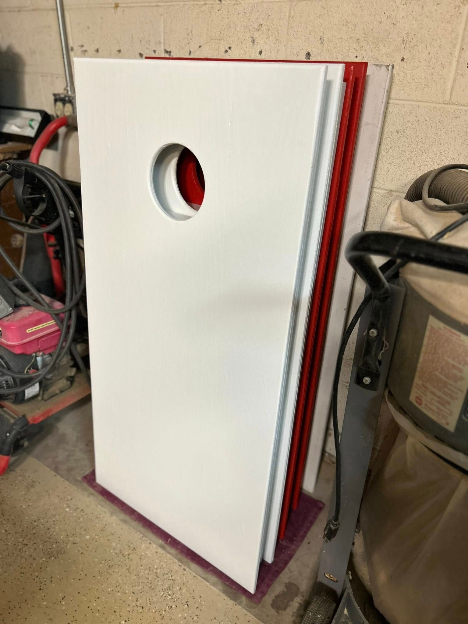 White cornhole boards stacked, one with a hole, in a garage.