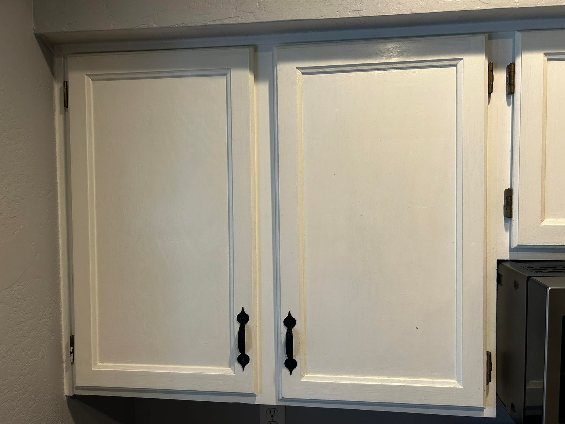 White kitchen cabinets with black handles, mounted on a gray wall.