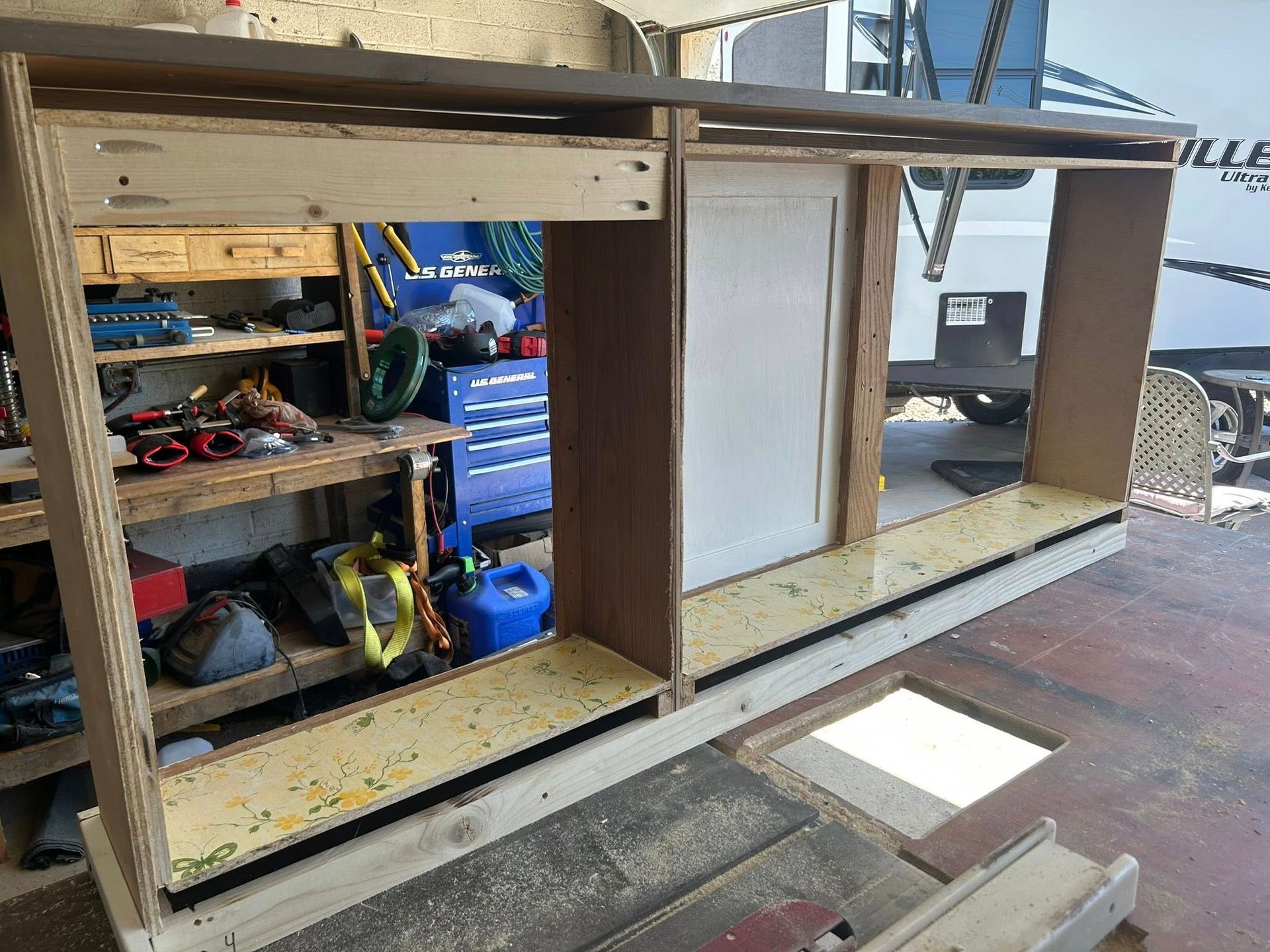 Wooden cabinet being built in a garage, with a door in the middle and open shelves on the sides.
