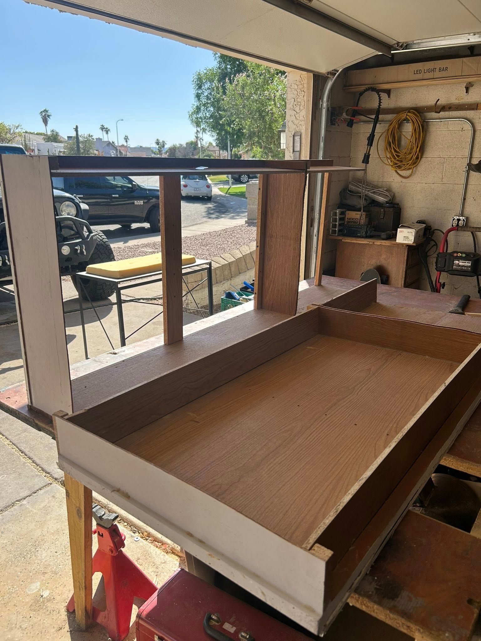 A partially built wooden cabinet on a workbench in a garage, with an open garage door in the background.