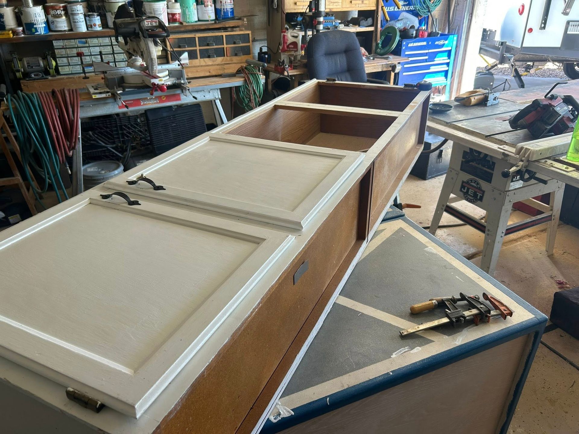 Cabinet with off-white doors, brown sides, and a partial interior on a workshop table.