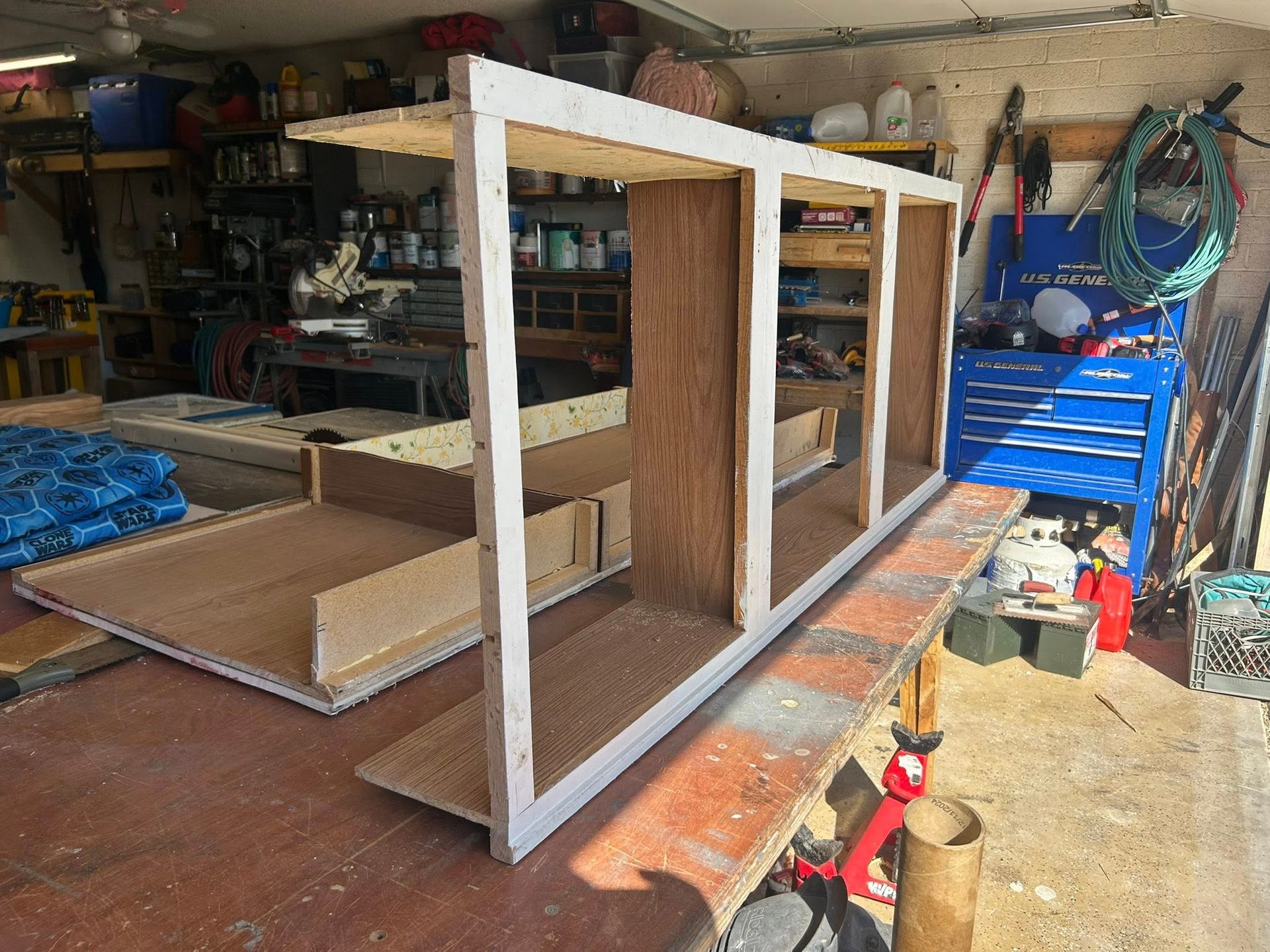 A partially constructed white-framed wooden structure, likely a cabinet, in a garage setting.