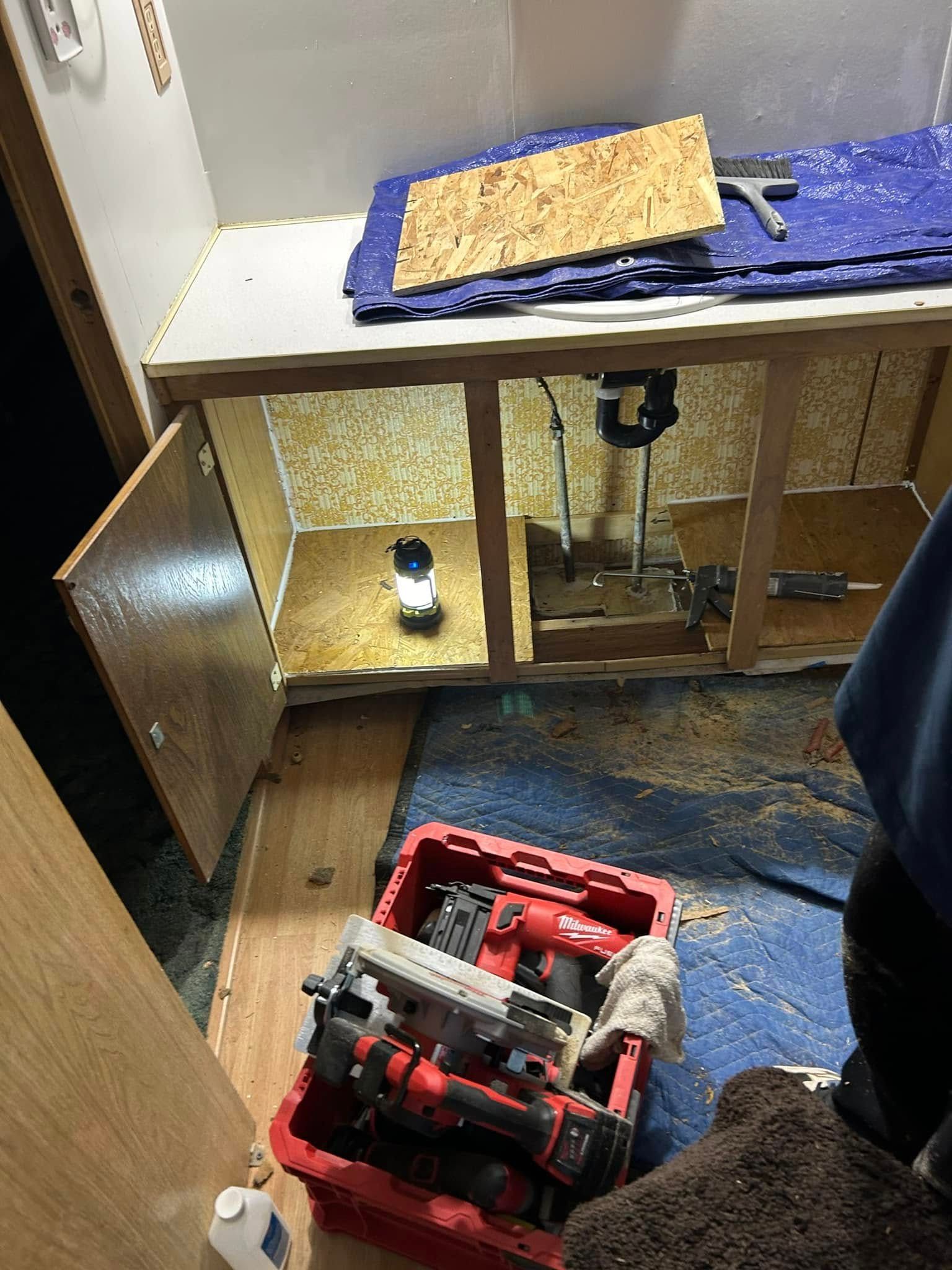 A workshop interior with a partially built wooden cabinet, tools in a red bin, and a work light.