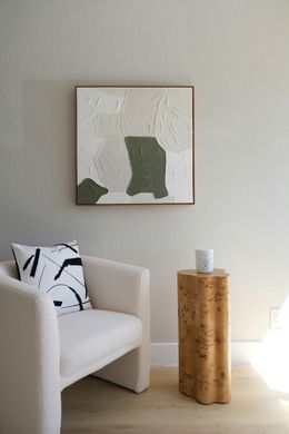 Cozy living space with a white armchair, art piece, and a side table. Neutral tones and textures.