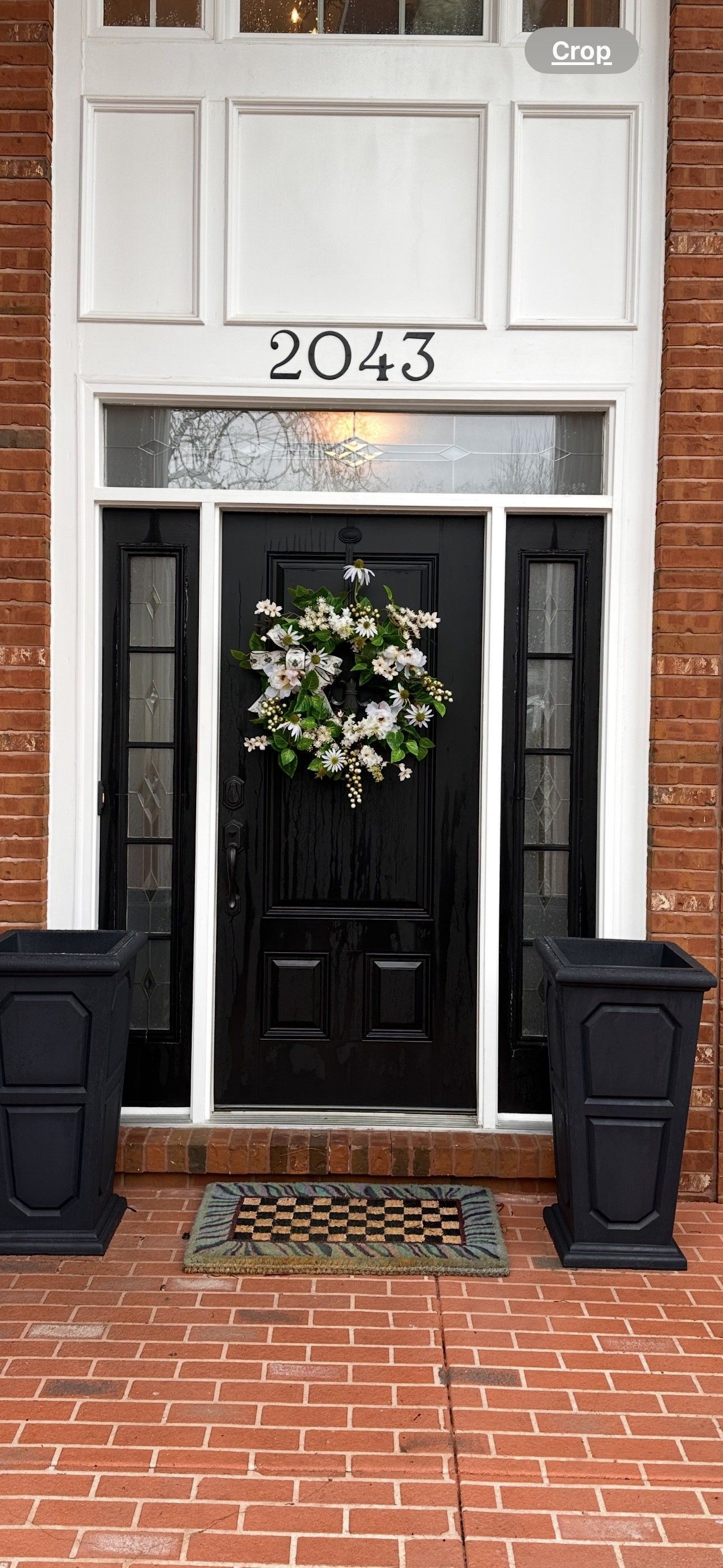 Black front door with wreath and address 2043; flanked by planters. Brick facade.