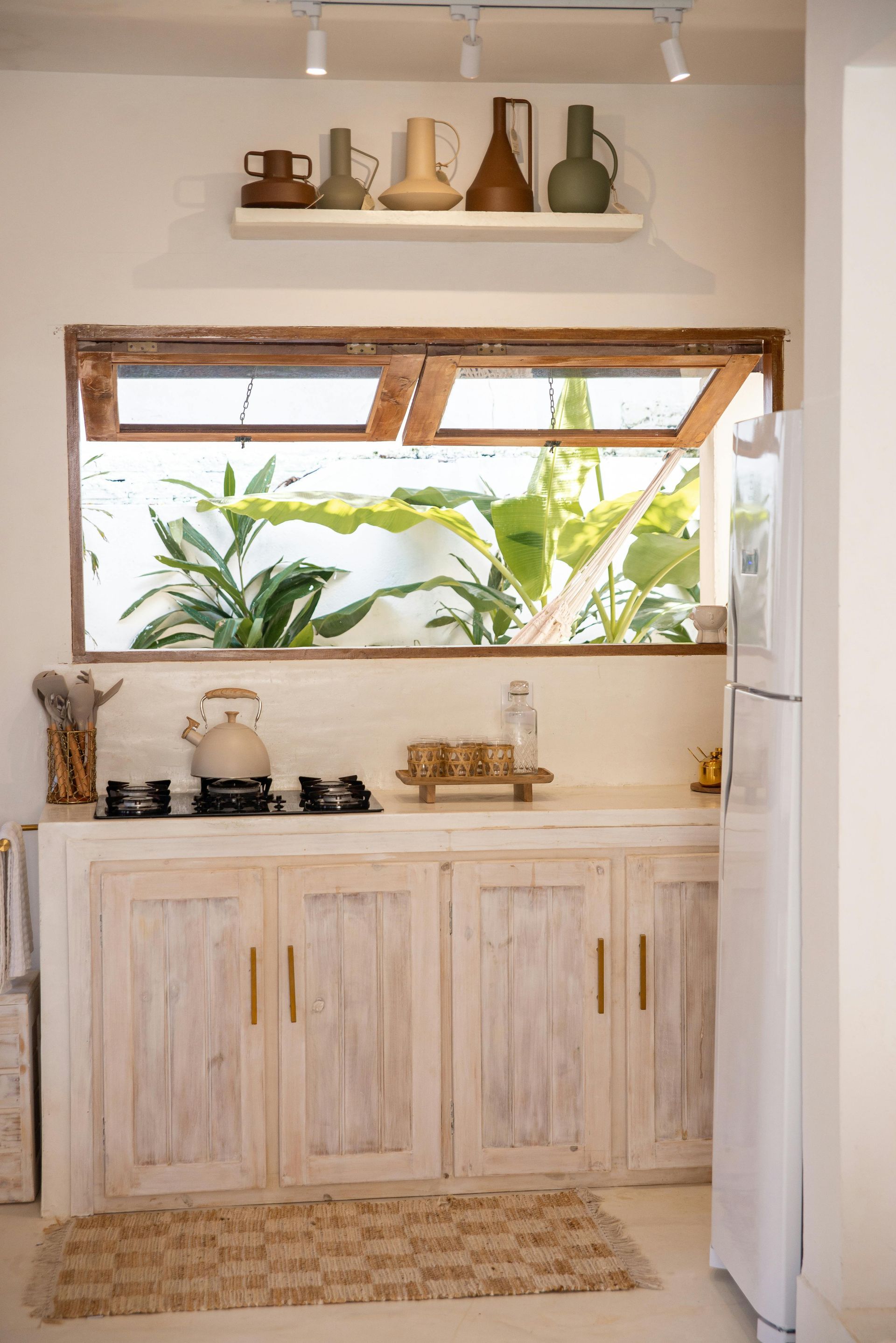 Beige kitchen with open window, rustic cabinets, and a view of lush greenery.