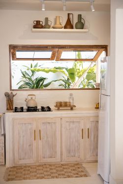 Kitchen with white cabinets, open window with plants visible, decorative vases on shelf, and stove.