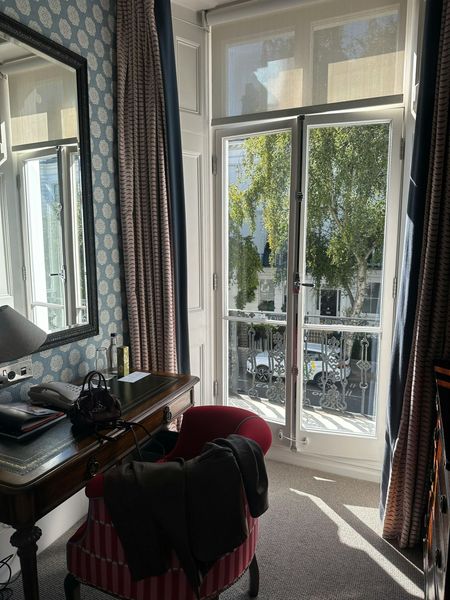 Interior view of a room with a desk, chair, mirror, and a window overlooking a street with trees.