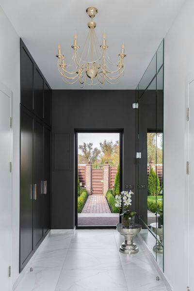 Hallway with black wall, wardrobes, gold chandelier, and view of a garden.