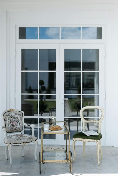 Two ornate chairs flank a gold bar cart in front of white French doors.