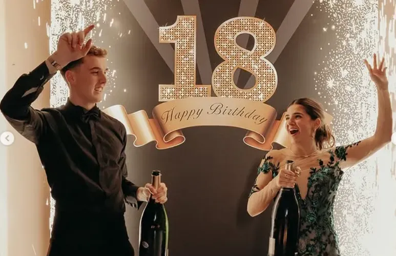 Due persone festeggiano il diciottesimo compleanno con champagne e coriandoli davanti a uno sfondo dorato.