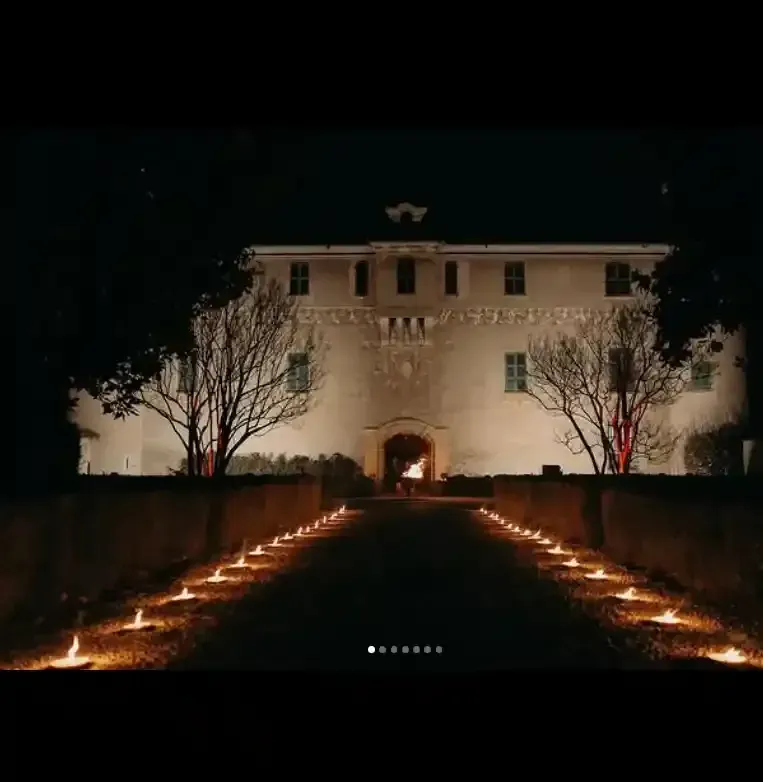 Villa bianca illuminata di notte, con un sentiero illuminato da candele che conduce all'ingresso.