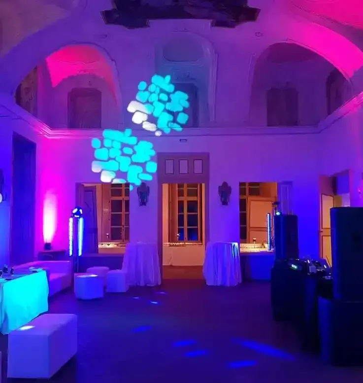 Sala eventi illuminata di viola con tavoli bianchi e decorazioni a soffitto blu brillante.