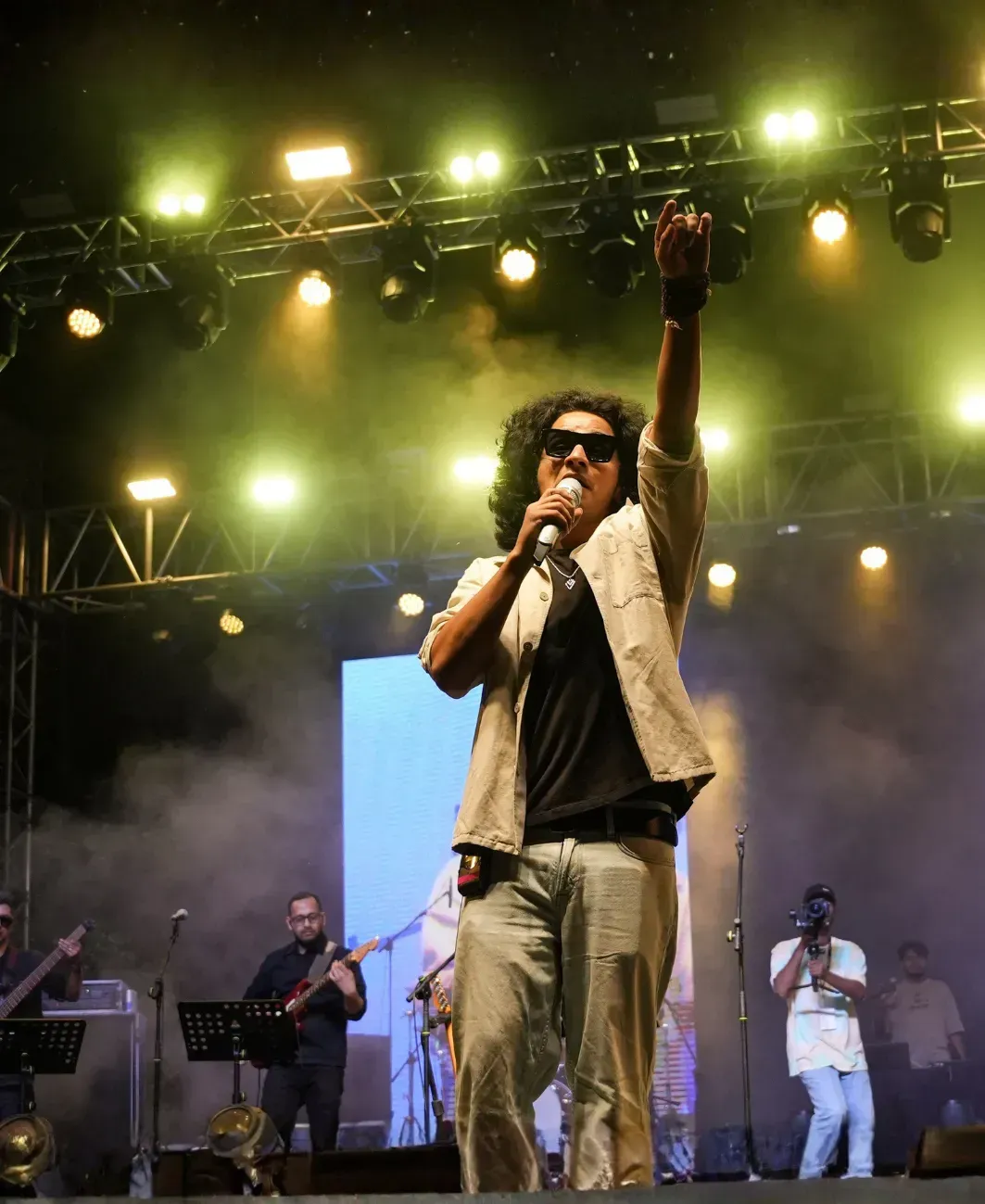 Cantante sul palco con microfono, braccio alzato sotto le luci intense del concerto e il fumo