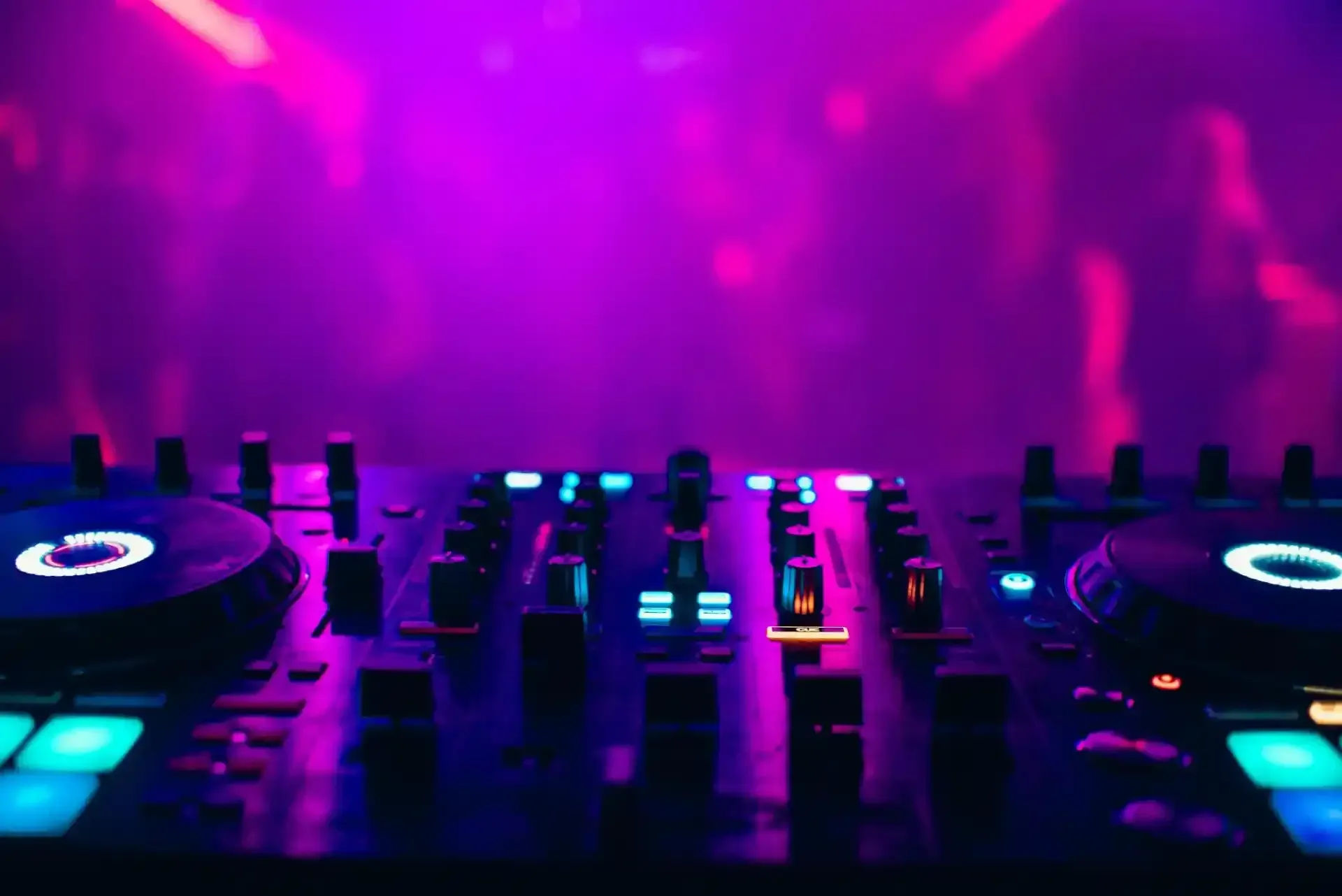 Mixer da DJ con comandi luminosi sotto luci da discoteca viola e rosa.