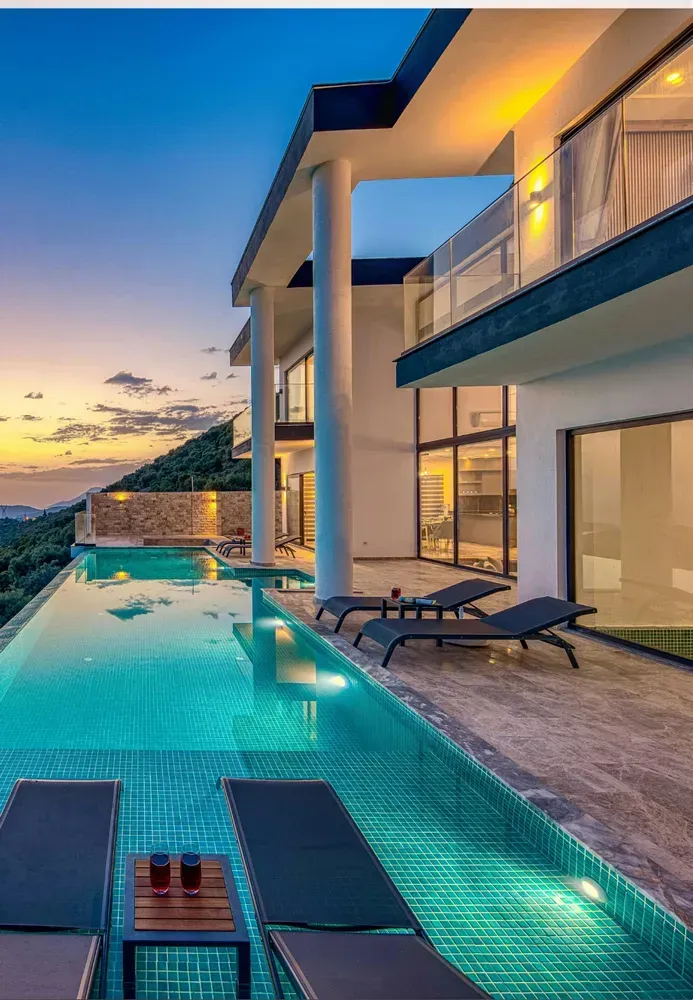 Villa di lusso con piscina a sfioro al tramonto, patio illuminato e vista sull'oceano.