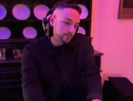 Una persona con una maglietta nera guarda in basso in una stanza illuminata di viola con decorazioni circolari alle pareti.