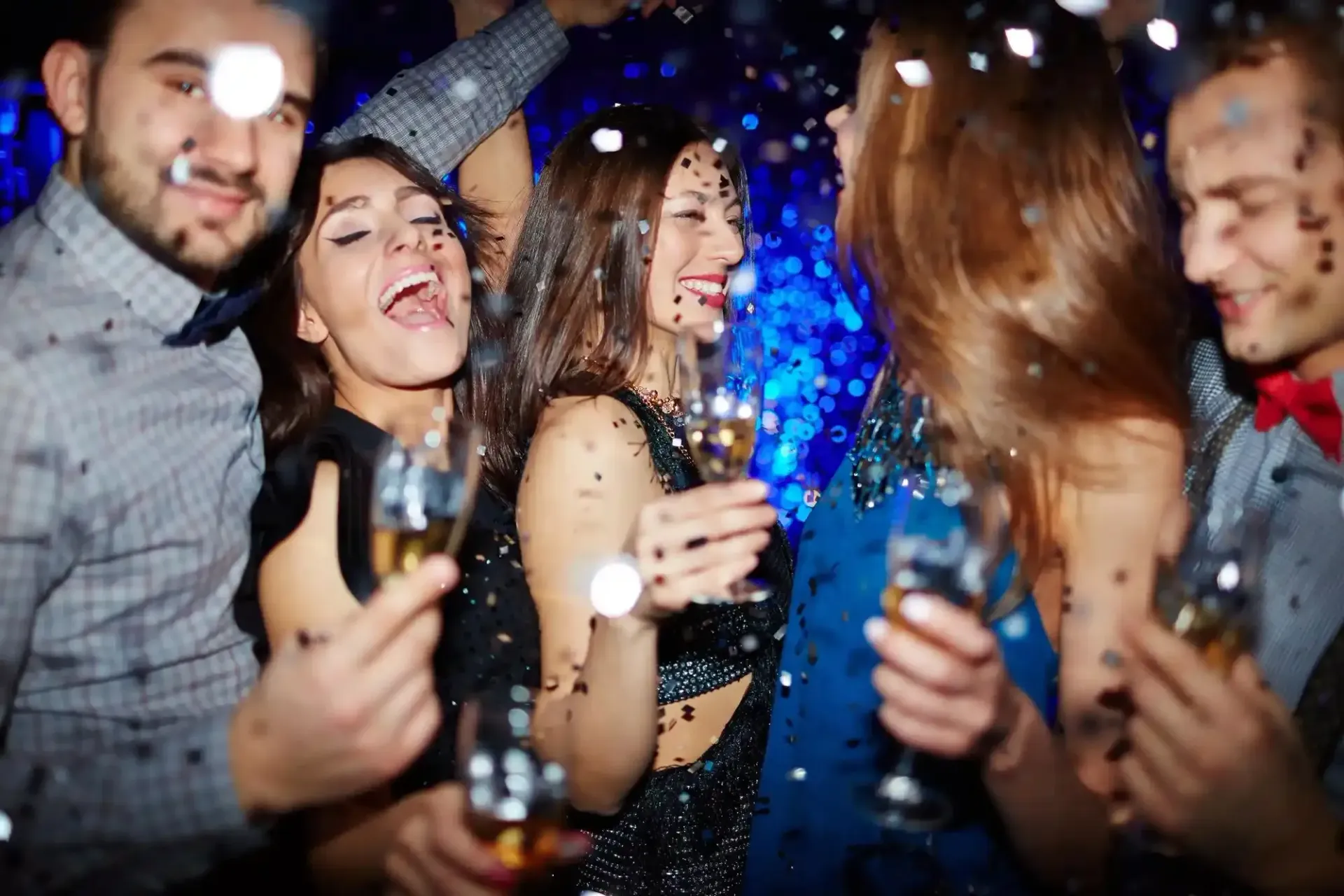 Amici che ballano e sorridono a una festa, con in mano dei drink sotto luci blu e bianche.