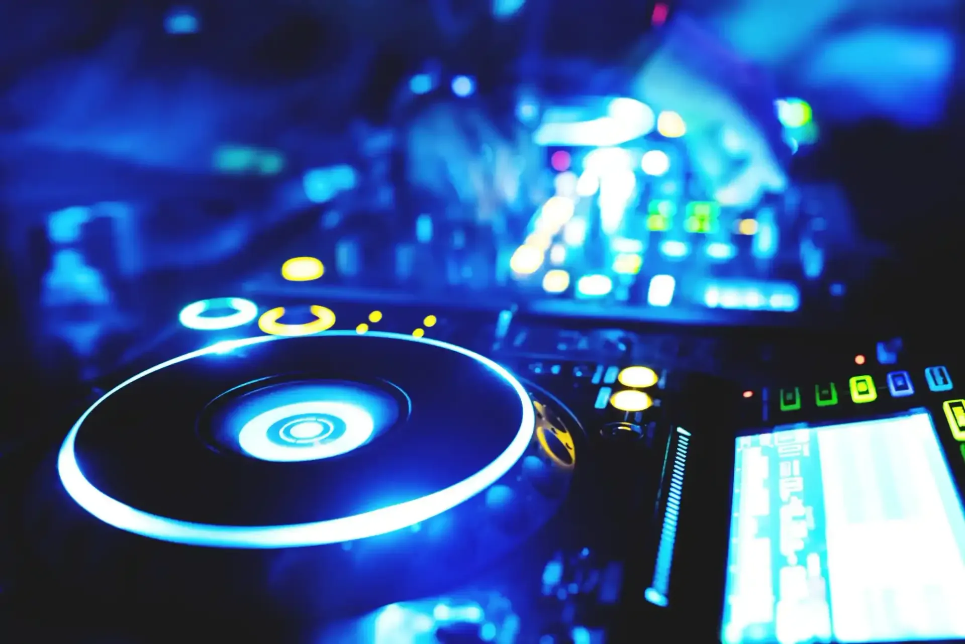 Giradischi e mixer da DJ illuminati da luci blu in un ambiente notturno buio.