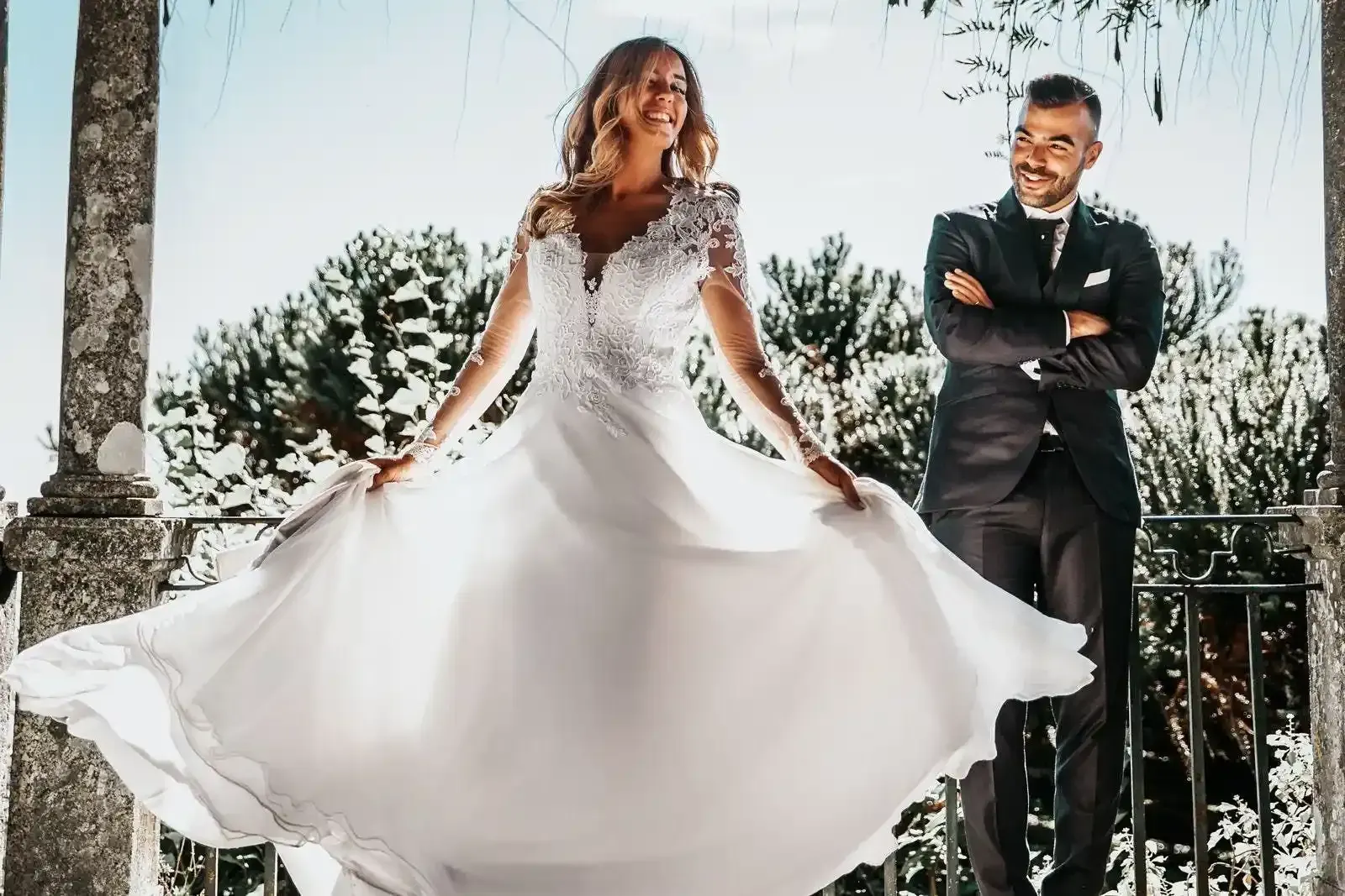 La sposa volteggia in un abito da sposa bianco mentre lo sposo le sorride accanto all'aperto.