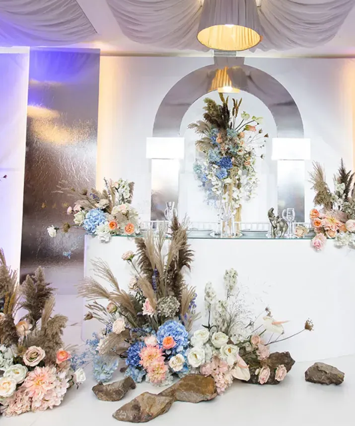 Elegante sfondo floreale per eventi con drappeggi bianchi, fiori dai colori pastello e uno specchio dorato al centro.
