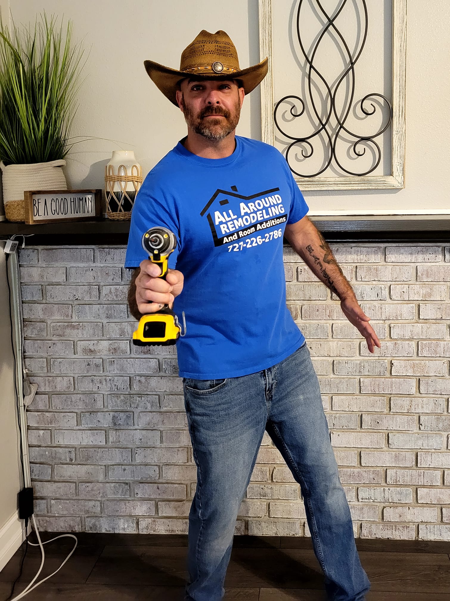 A man wearing a cowboy hat and a blue shirt is holding a drill.