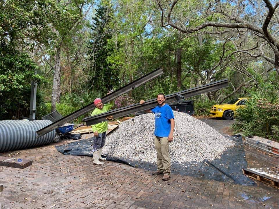 Two men are standing next to a pile of gravel and holding a piece of metal.