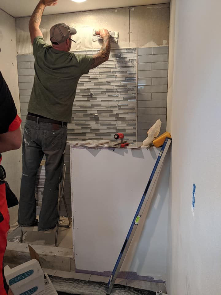 A man is installing tiles on a wall in a bathroom.