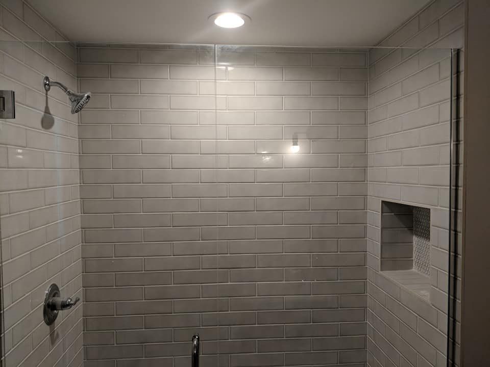 A shower with white tiles and a glass door.