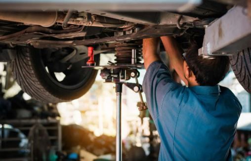 Mechanic working under a car lifted on a hoist in a repair shop. He is wearing a blue shirt.