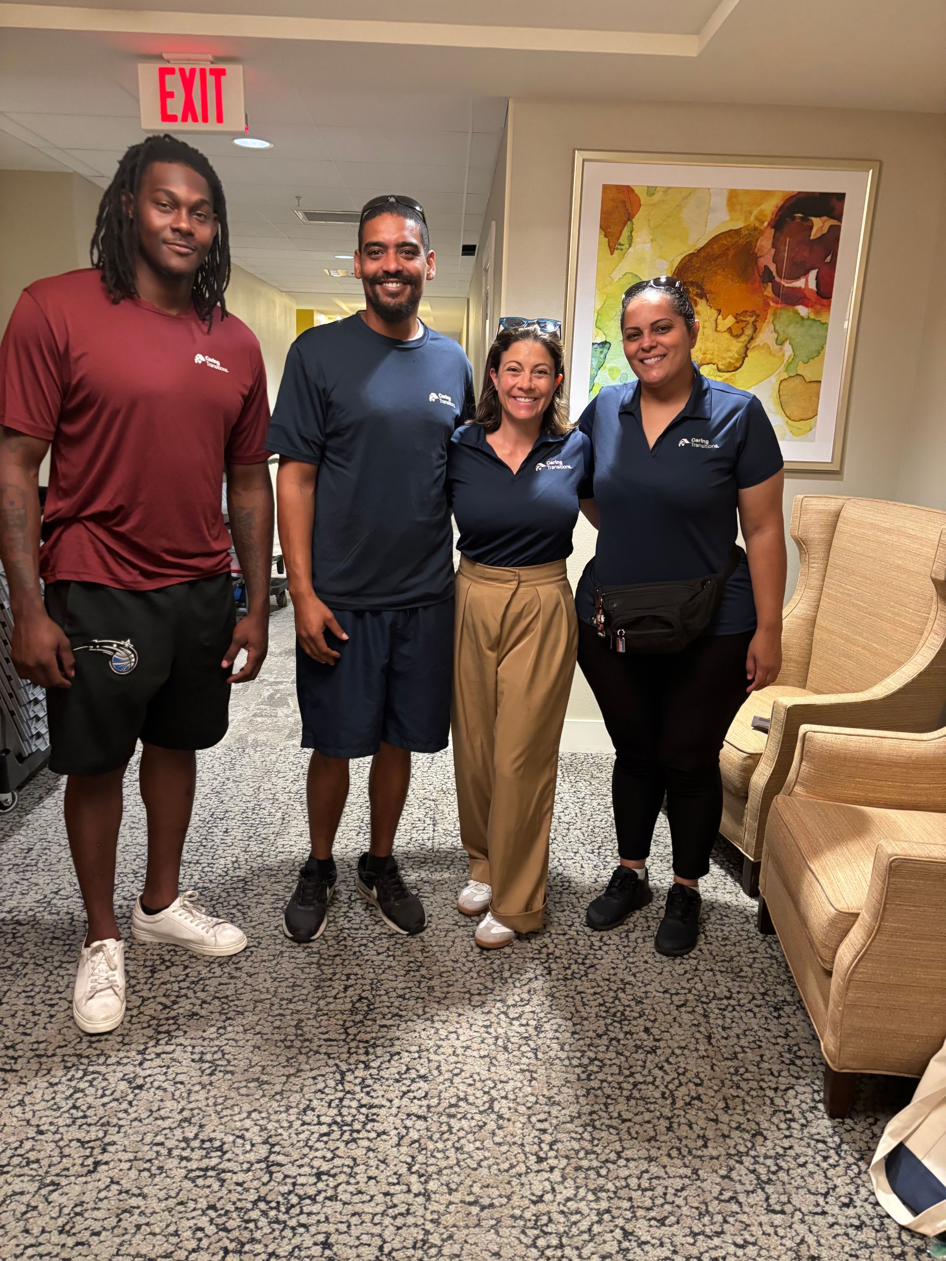 A group of people are posing for a picture in a hallway with an exit sign above them.