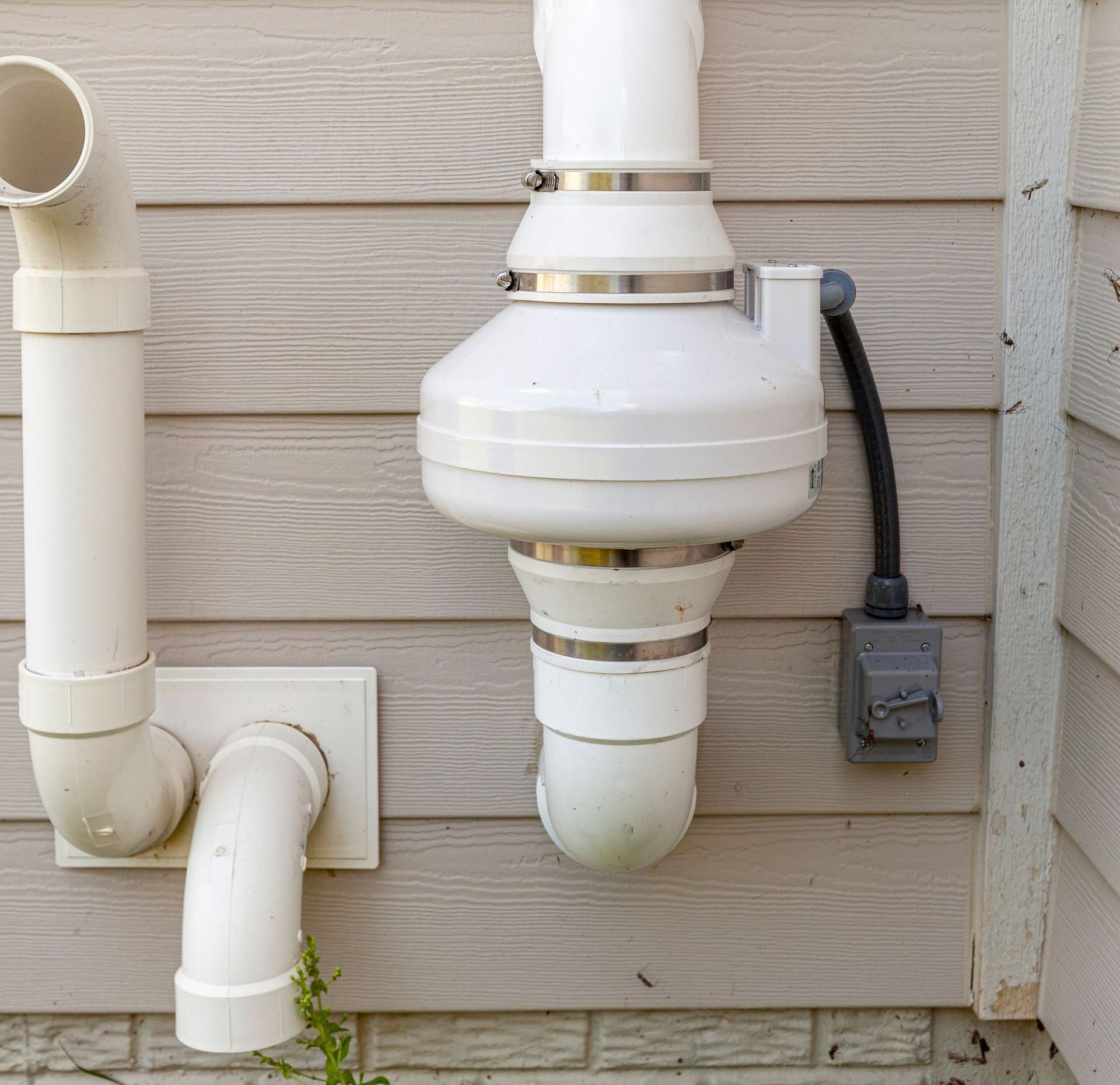 A white radon mitigation system is attached to the side of a house