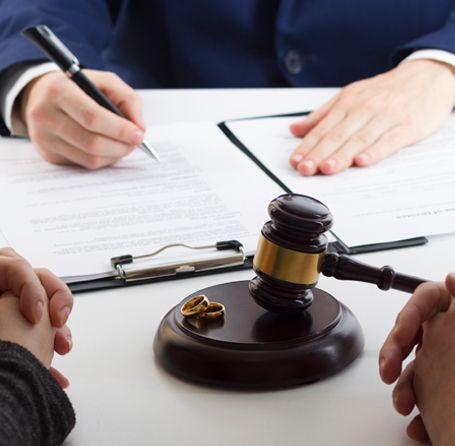 Divorce proceeding: Wedding rings, gavel, legal documents, hands, and person writing.