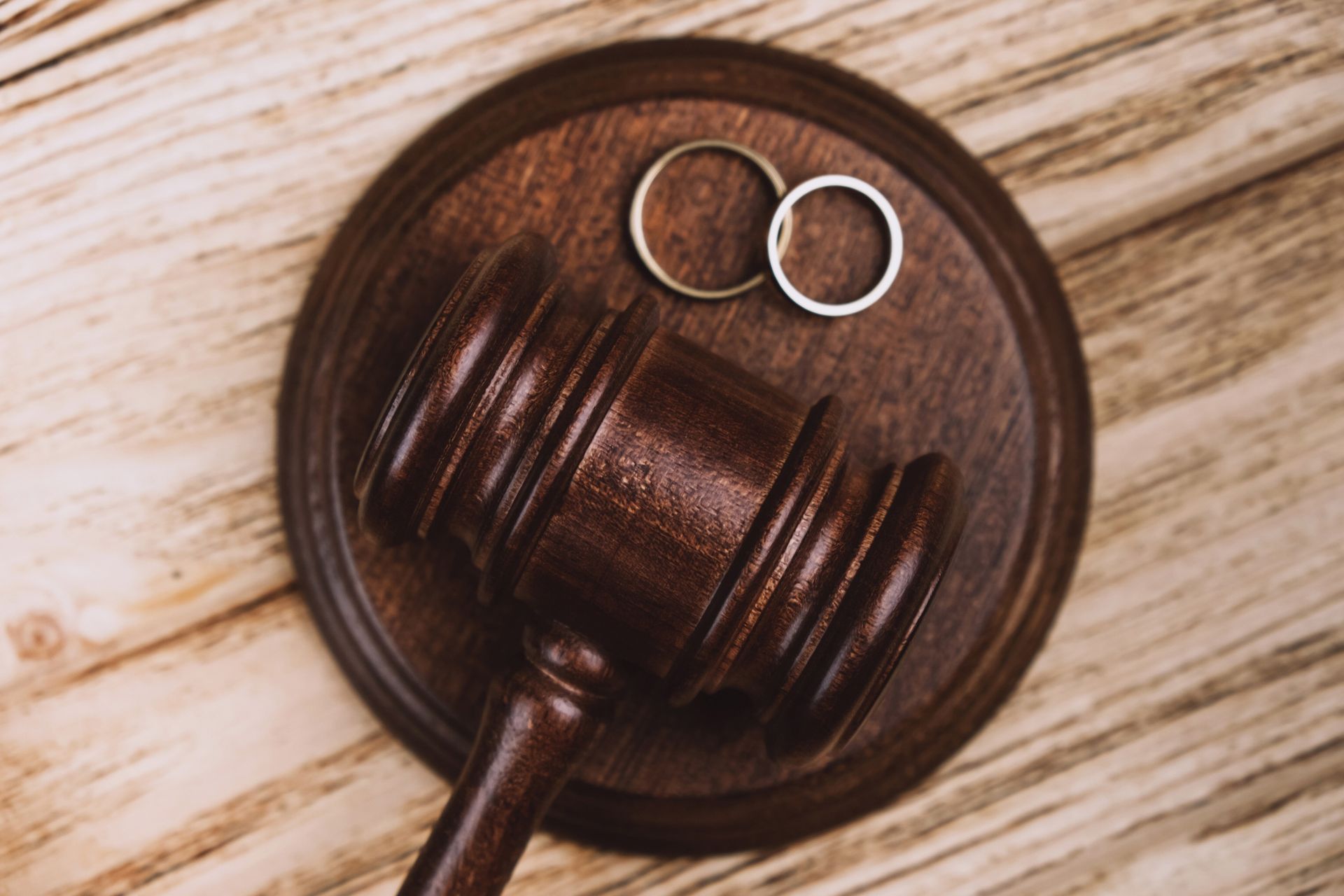 Wooden gavel and two wedding rings on a wooden surface.