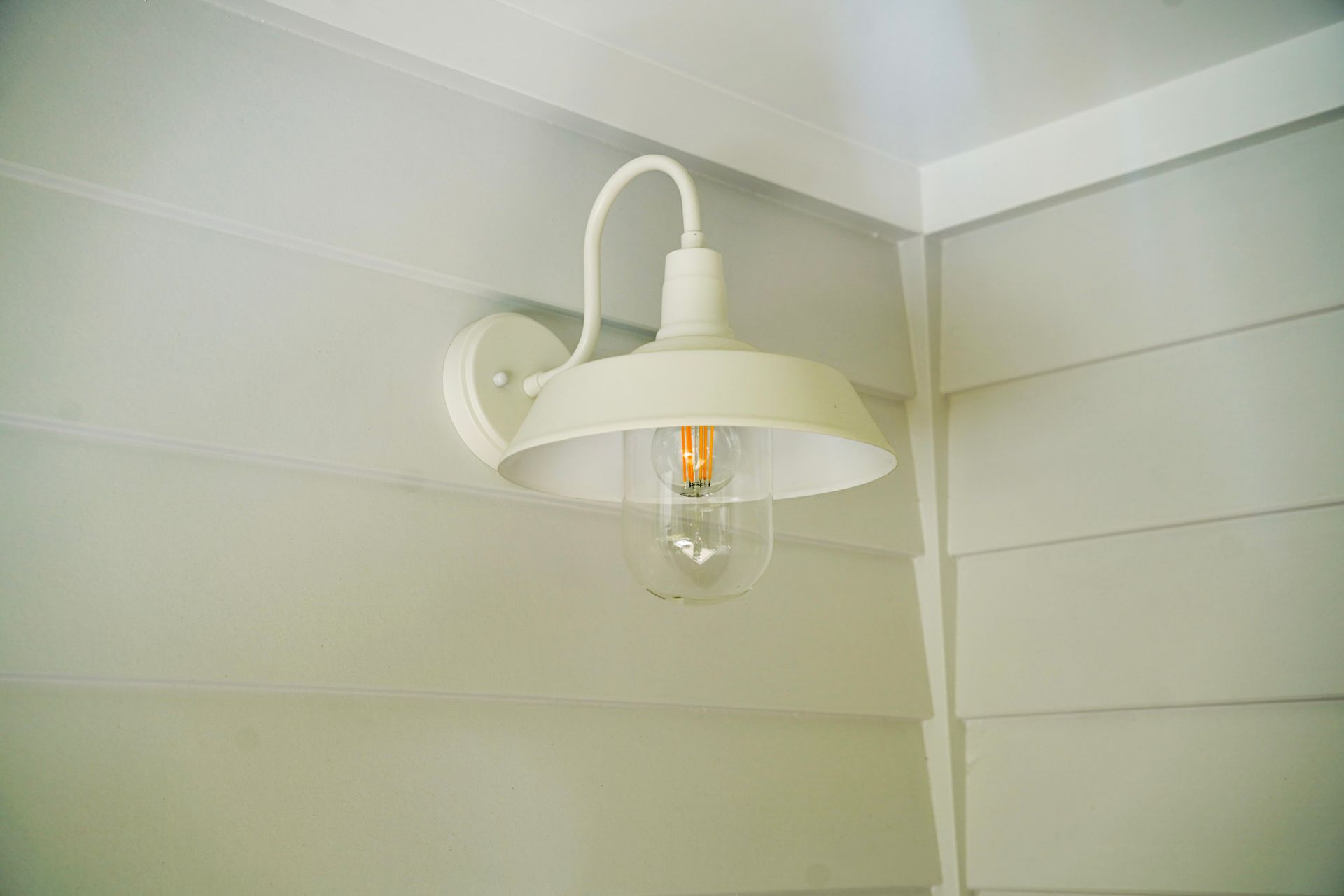 White barn-style light fixture on a white-paneled wall, corner of a building.