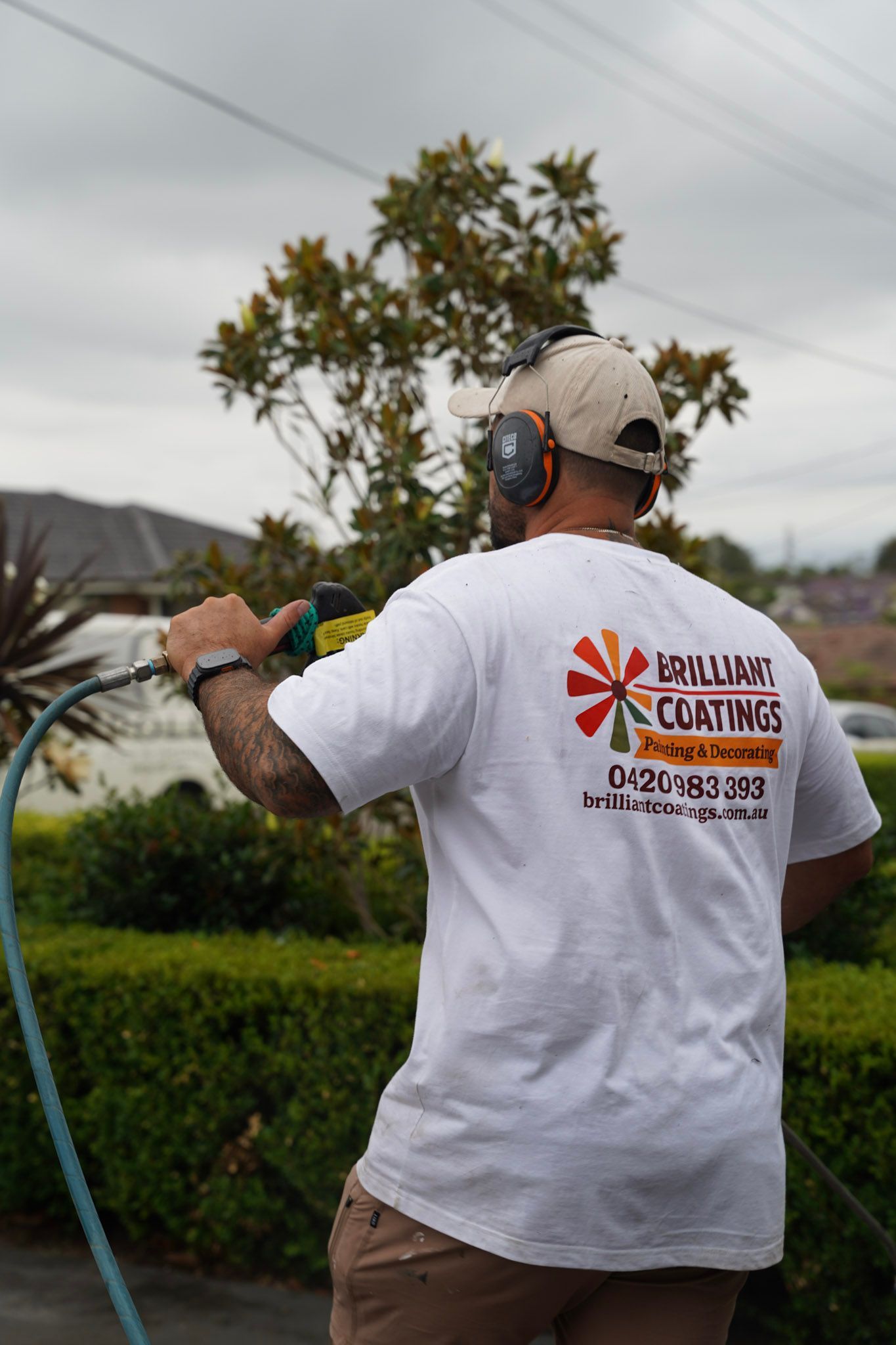 Man in white shirt with company logo operates a hose outside.