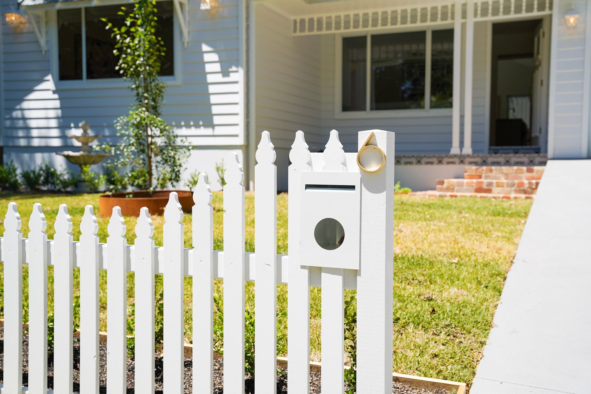 White picket fence with mailbox, in front of a white house with a brick entry.